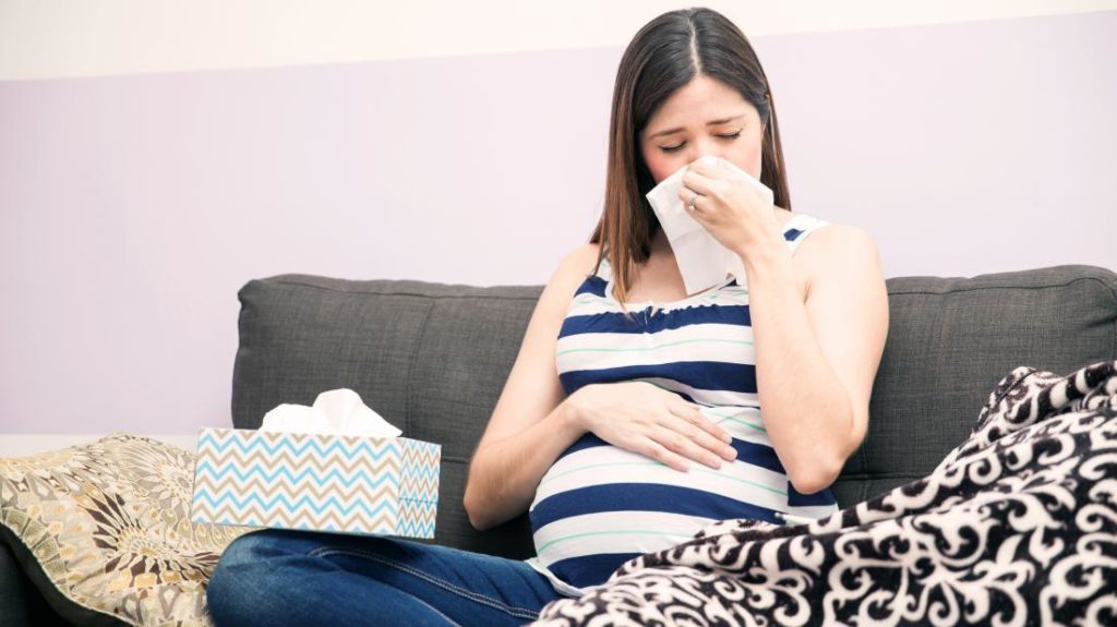 Una mujer sonándose la nariz porque tiene gripe durante el embarazo.