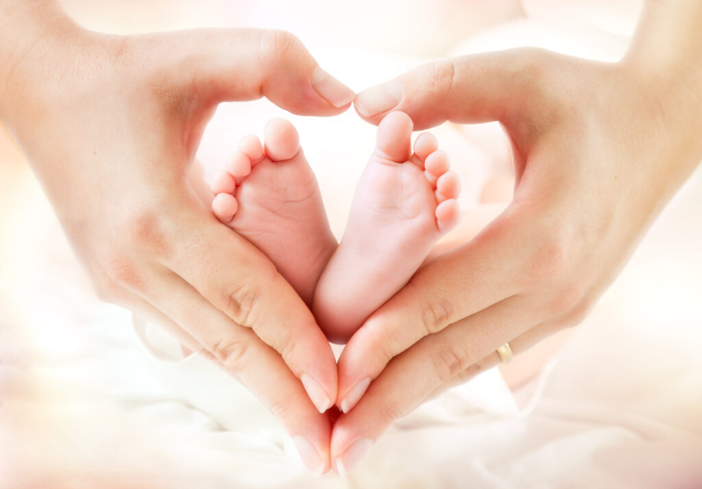 A close-up of an adult's hands forming a heart shape around a baby's tiny feet, symbolizing love and care.