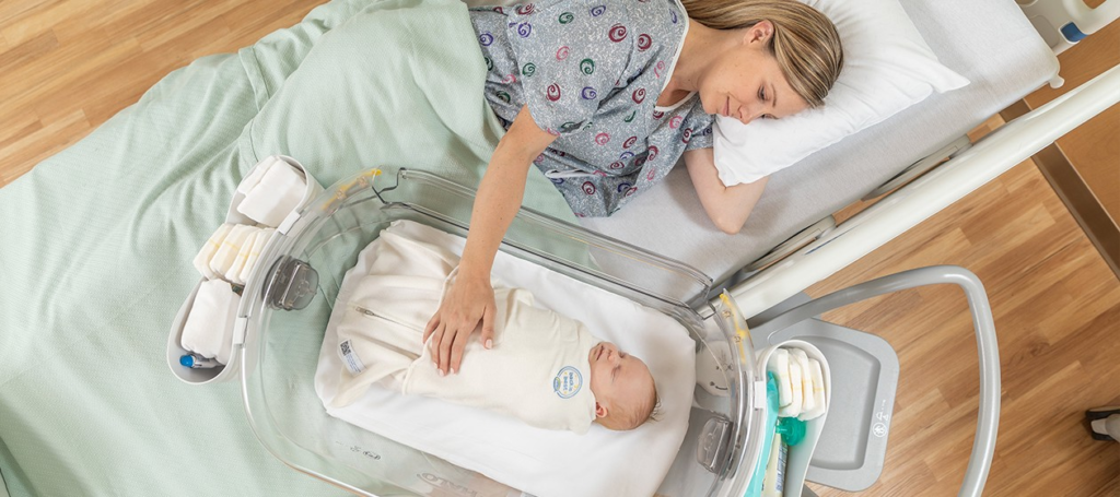 A new mother watching their newborn - Joy of Life Surrogacy