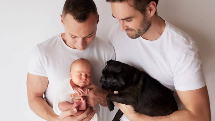 padre del mismo sexo sosteniendo a su bebé y a su cachorro - Joy of Life® Subrogación