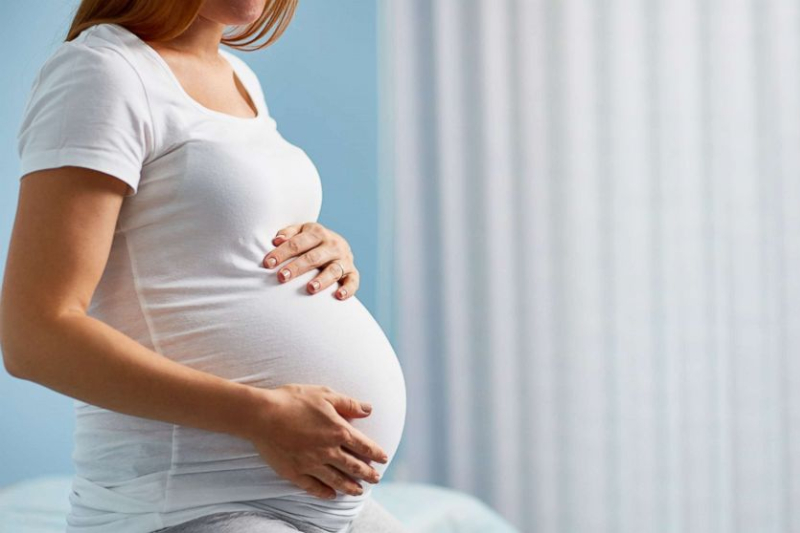 一位怀孕的妈妈穿着白色T恤坐在床上 - Joy of Life 代孕