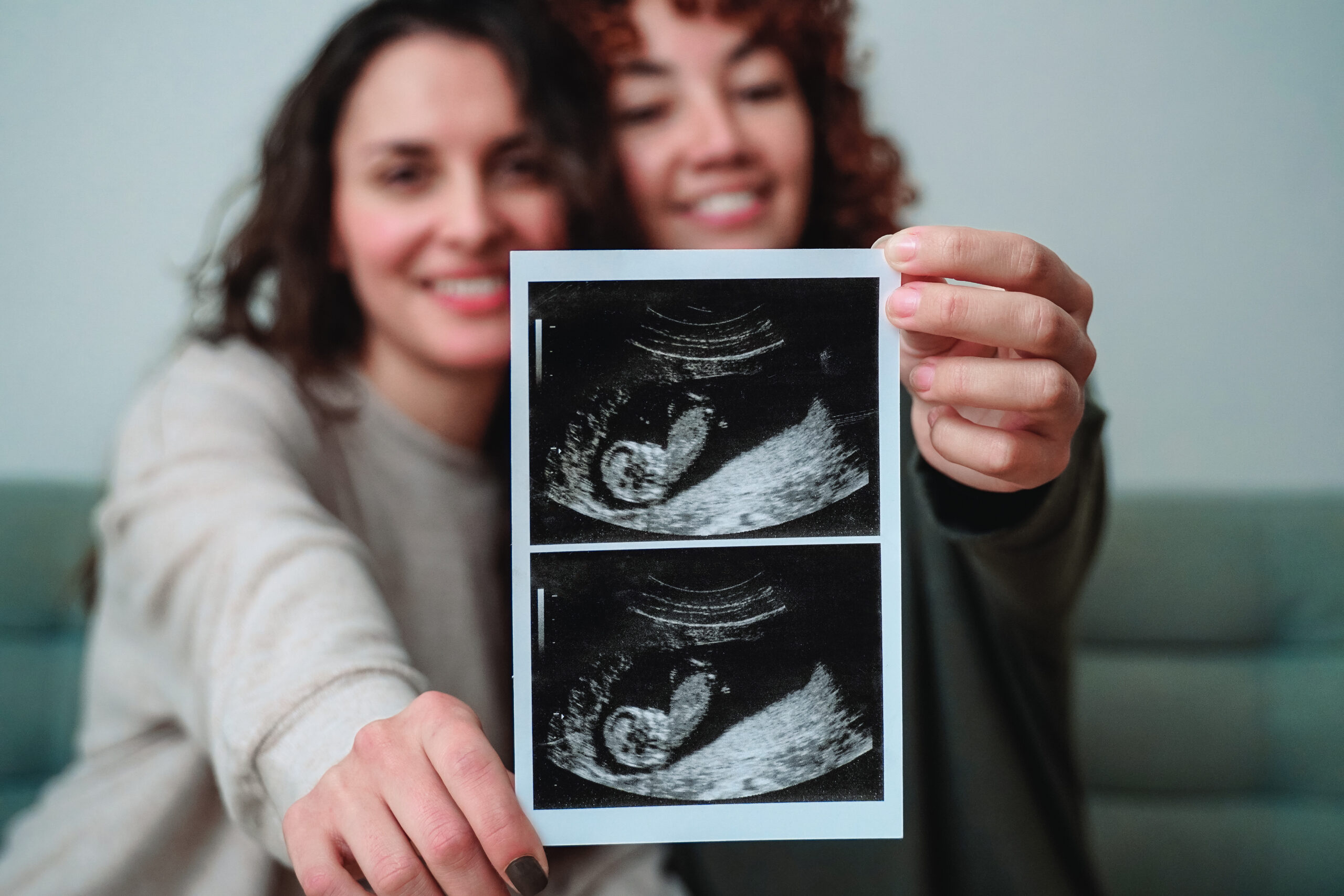 A surrogate mother and her friend, the intended parent, hold up an ultrasound of the growing fetus.