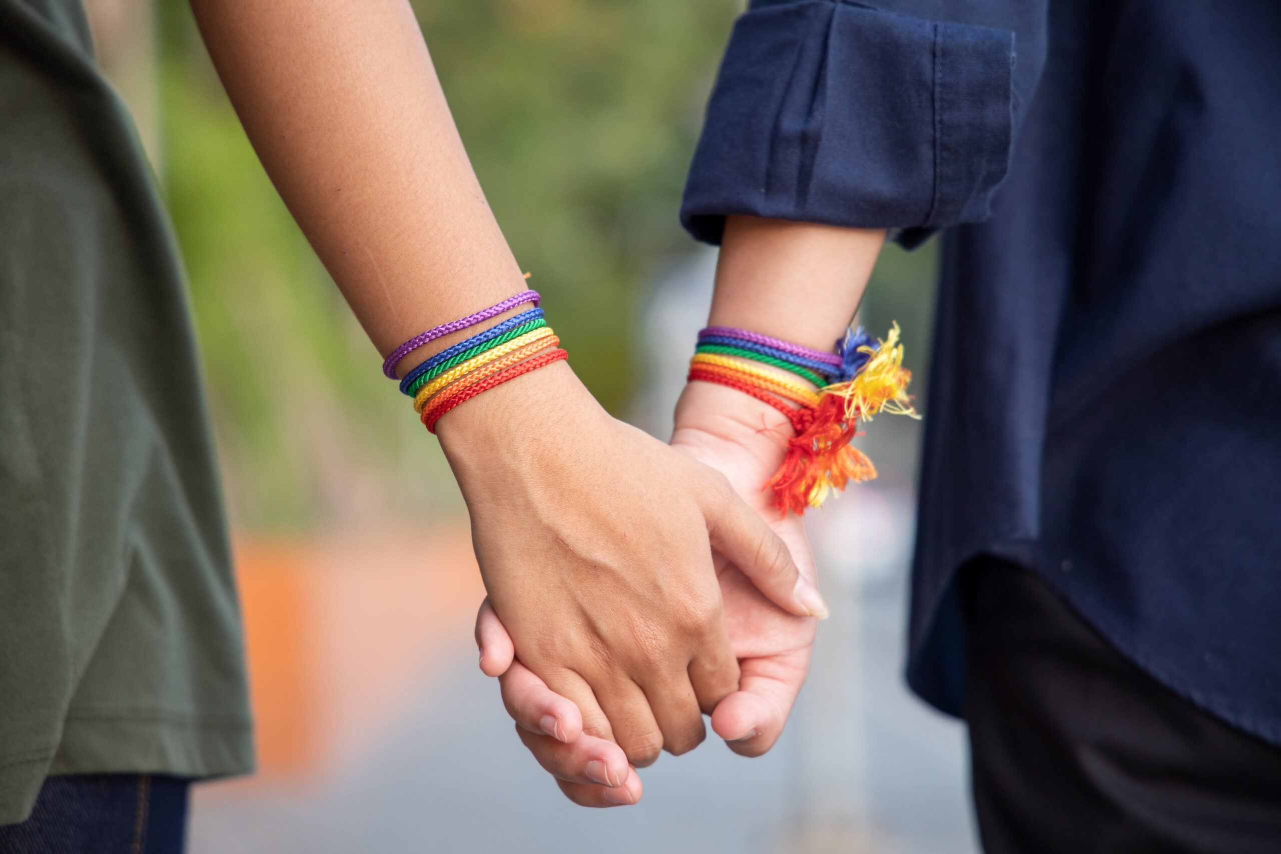 Two individuals walking hand in hand, wearing rainbow-colored bracelets.