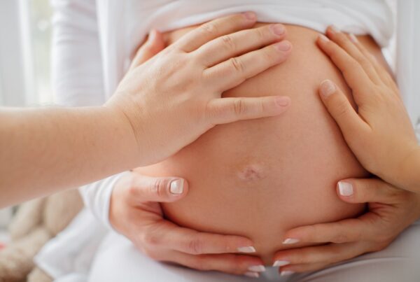 A close-up of a pregnant person's belly cradled by their hands and another's hands.