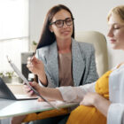 Surrogacy agency coordinator reviews paperwork with a pregnant woman in a bright office, offering guidance as they look over a clipboard together.