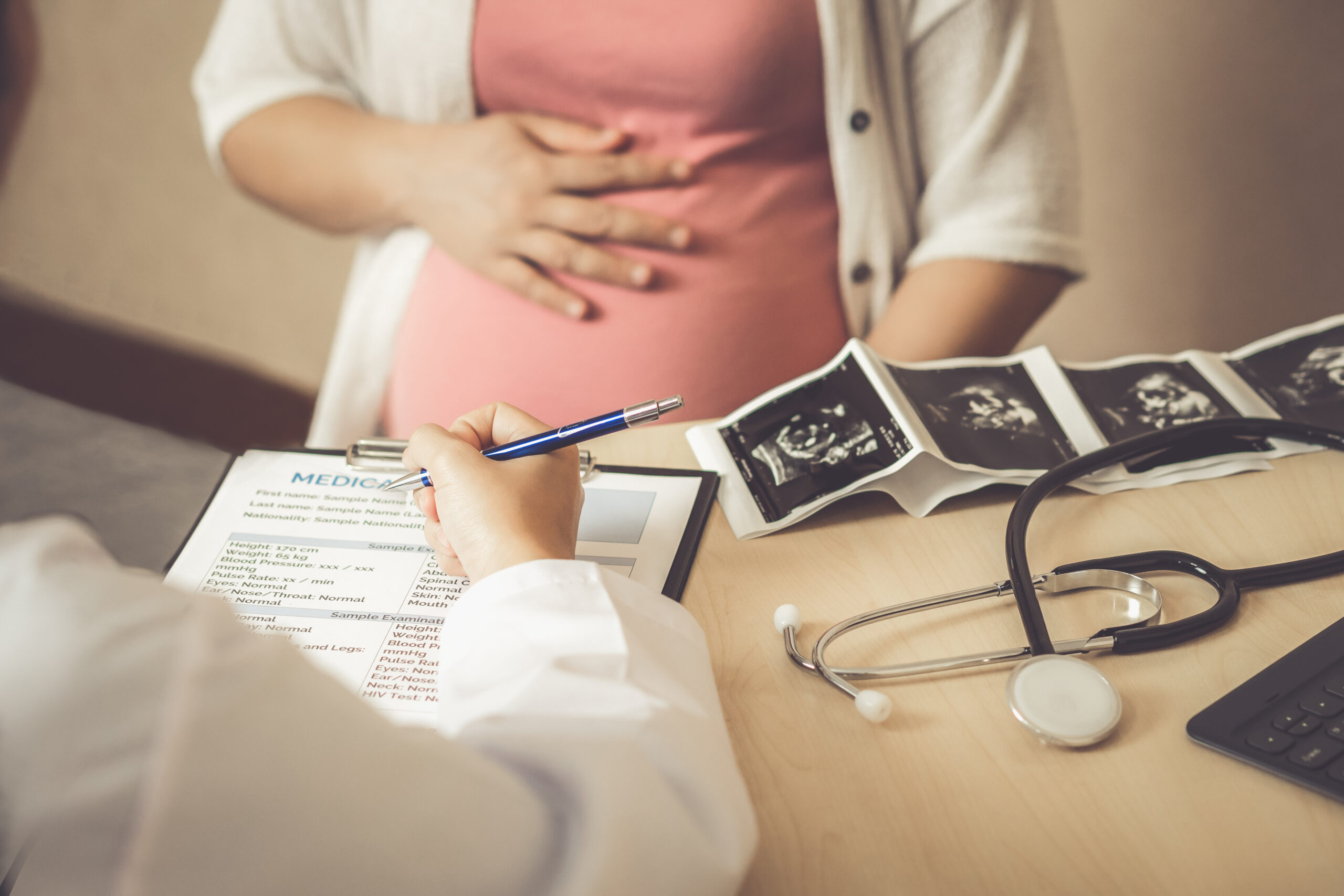 A close-up shot of a pregnant woman sitting across a from a doctor who is holding a clipboard with the woman's medical information.