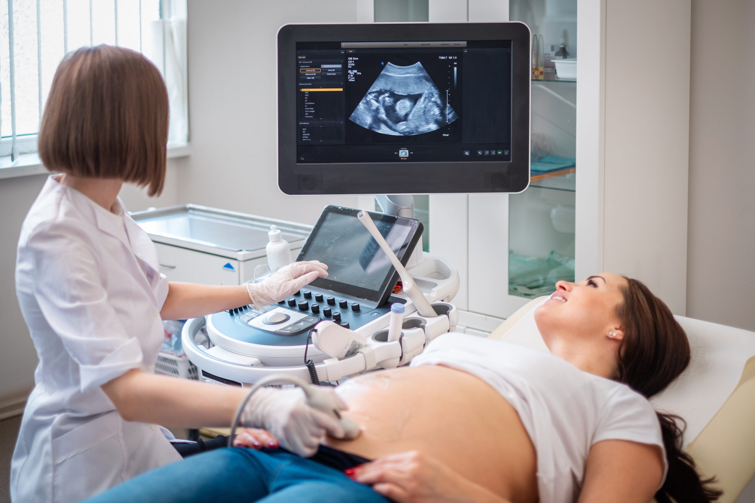 Pregnant woman undergoing an ultrasound scan performed by a medical professional, with the baby's image visible on the monitor.