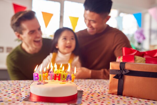 Familia con dos papás celebrando el cumpleaños de su hija en casa con pastel y fiesta