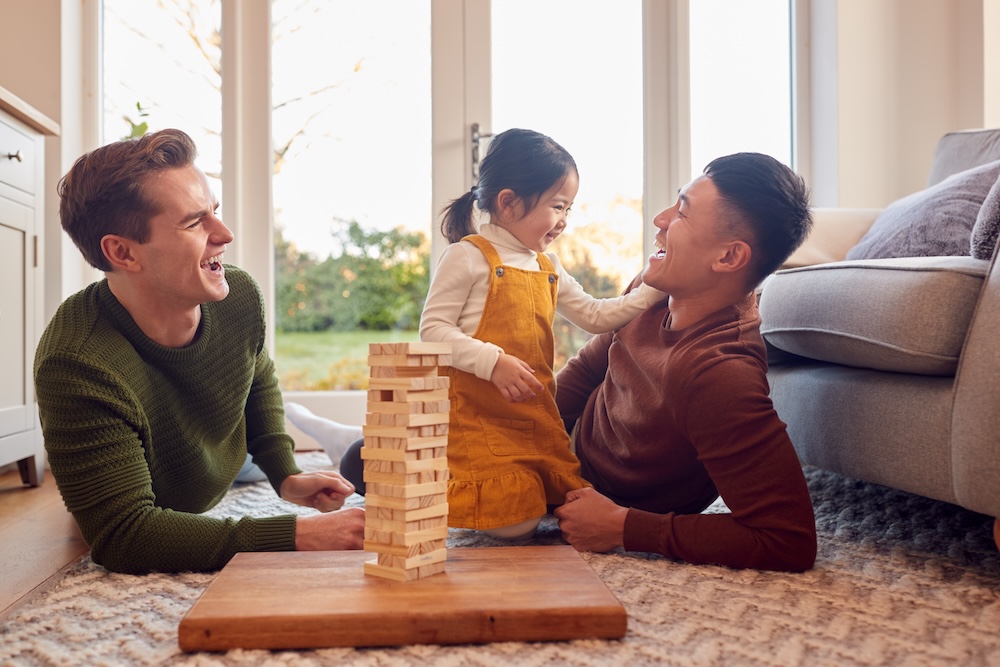 Familia con dos papás jugando con su hija en casa apilando ladrillos de madera en una torre