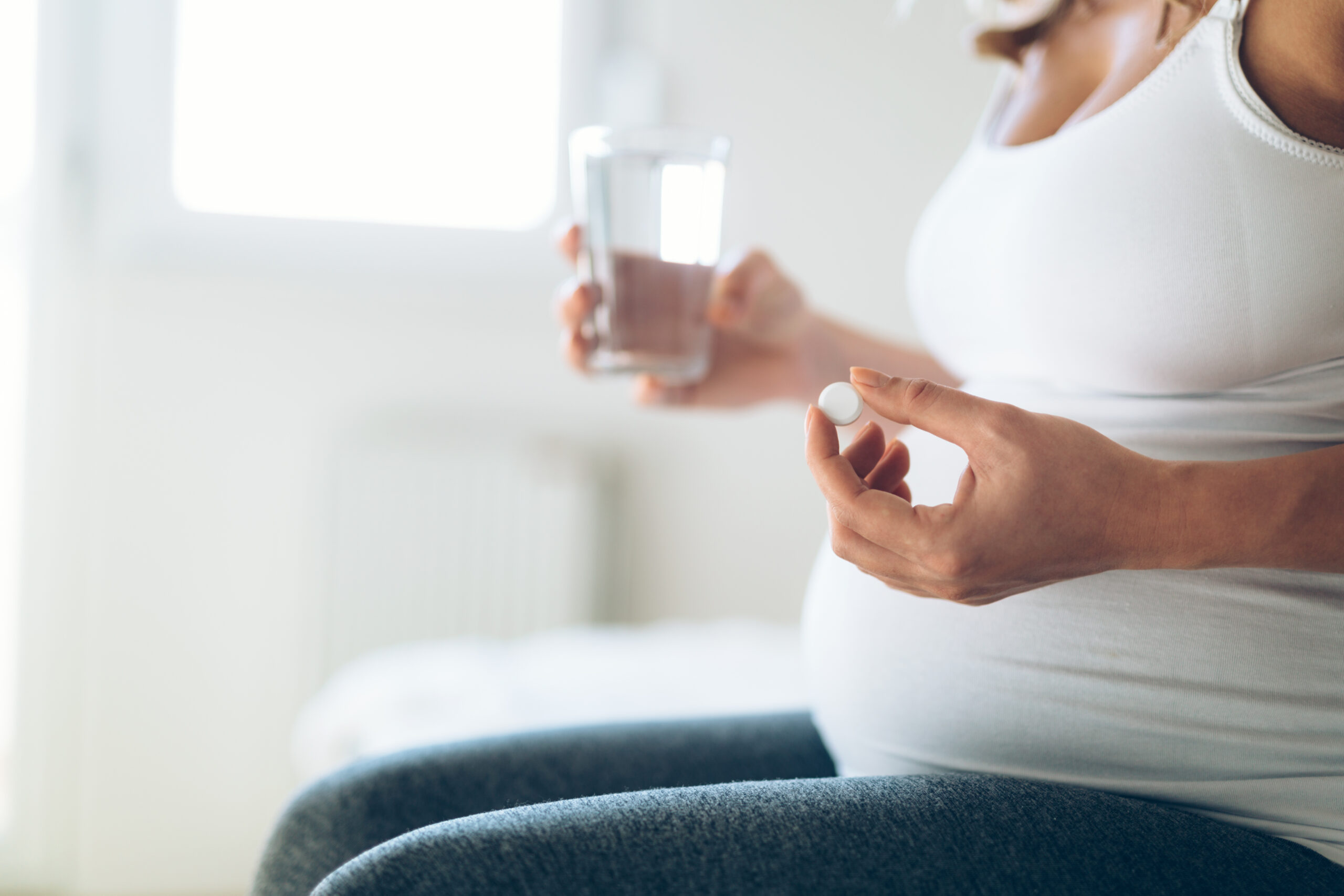 Pregnant woman holding a pill and a glass of water