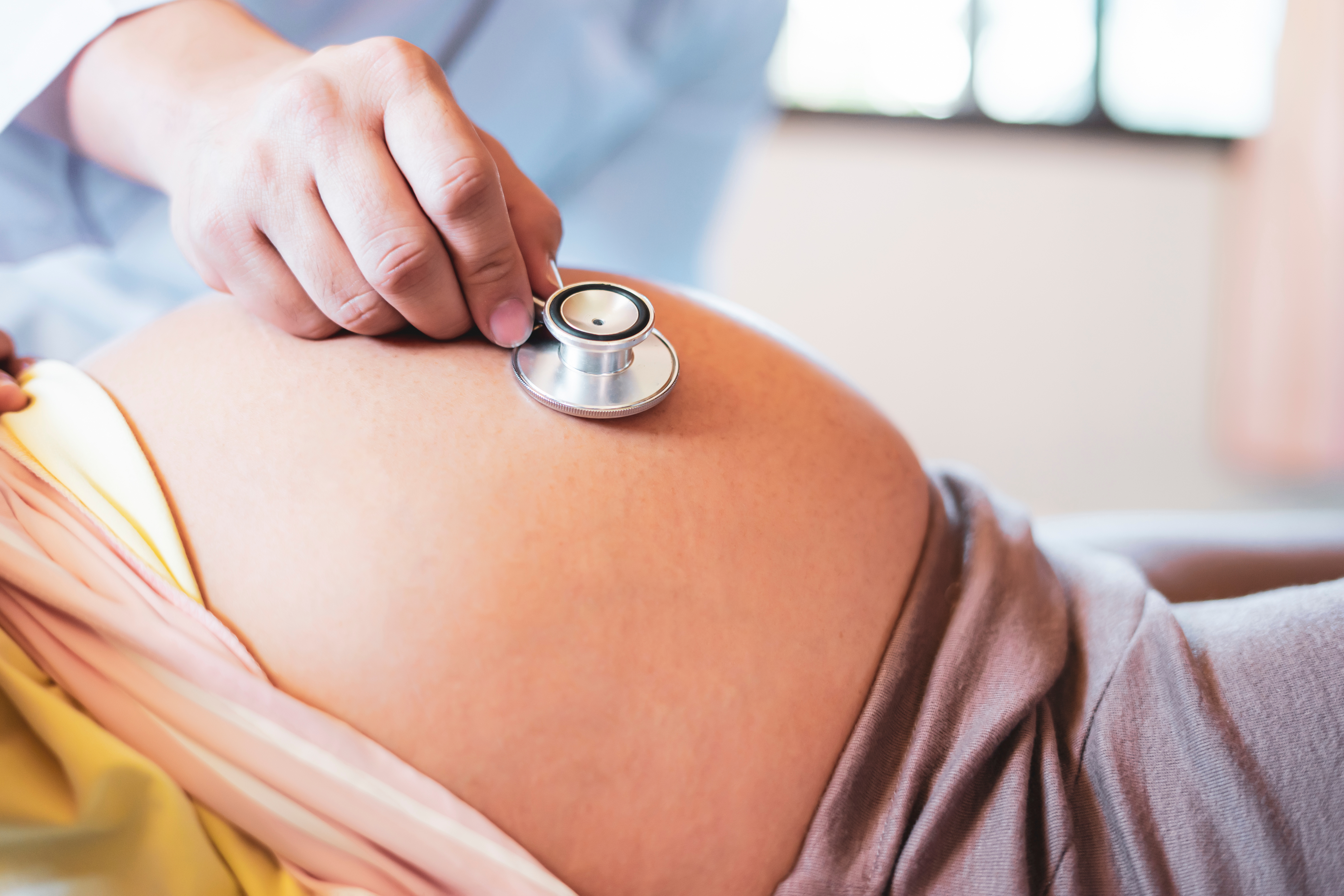 A close-up shot of a pregnant woman's stomach while a doctor listens to the baby's heartbeat through a stethoscope.