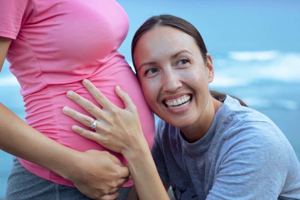 一位女士抱着代孕妈妈怀孕的肚子，笑容满面。
