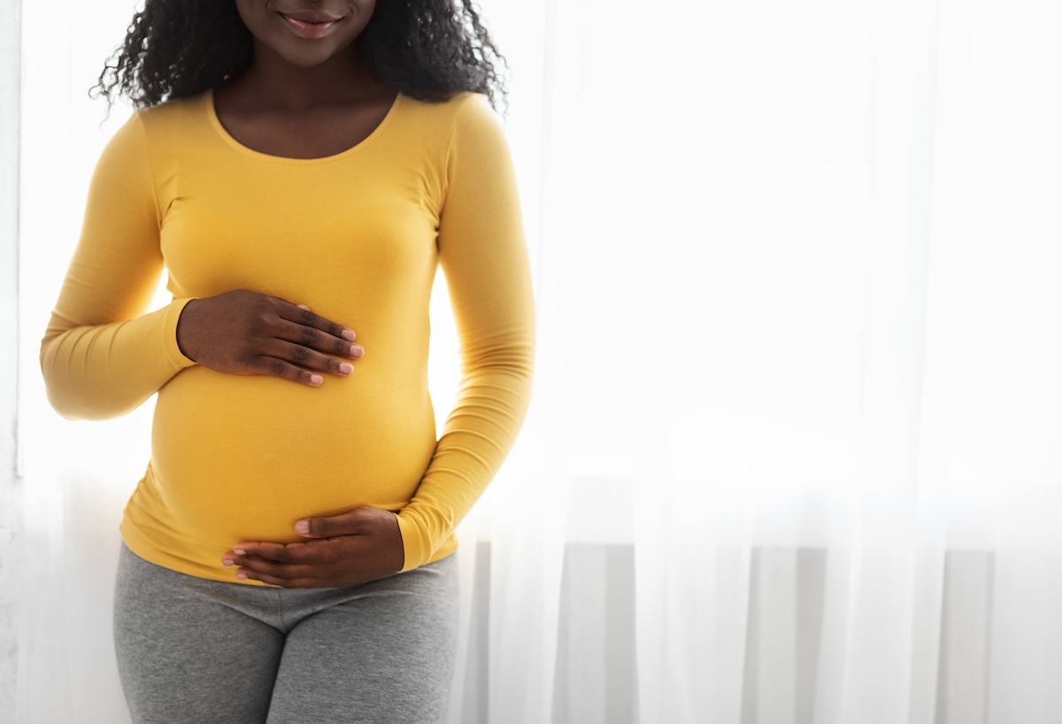 Pregnant person in yellow clothing cradling their belly with both hands.