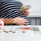 A surrogate mother in a striped dress sitting at a table with a piggy bank, budgeting funds from her surrogacy compensation for taxes and expenses.