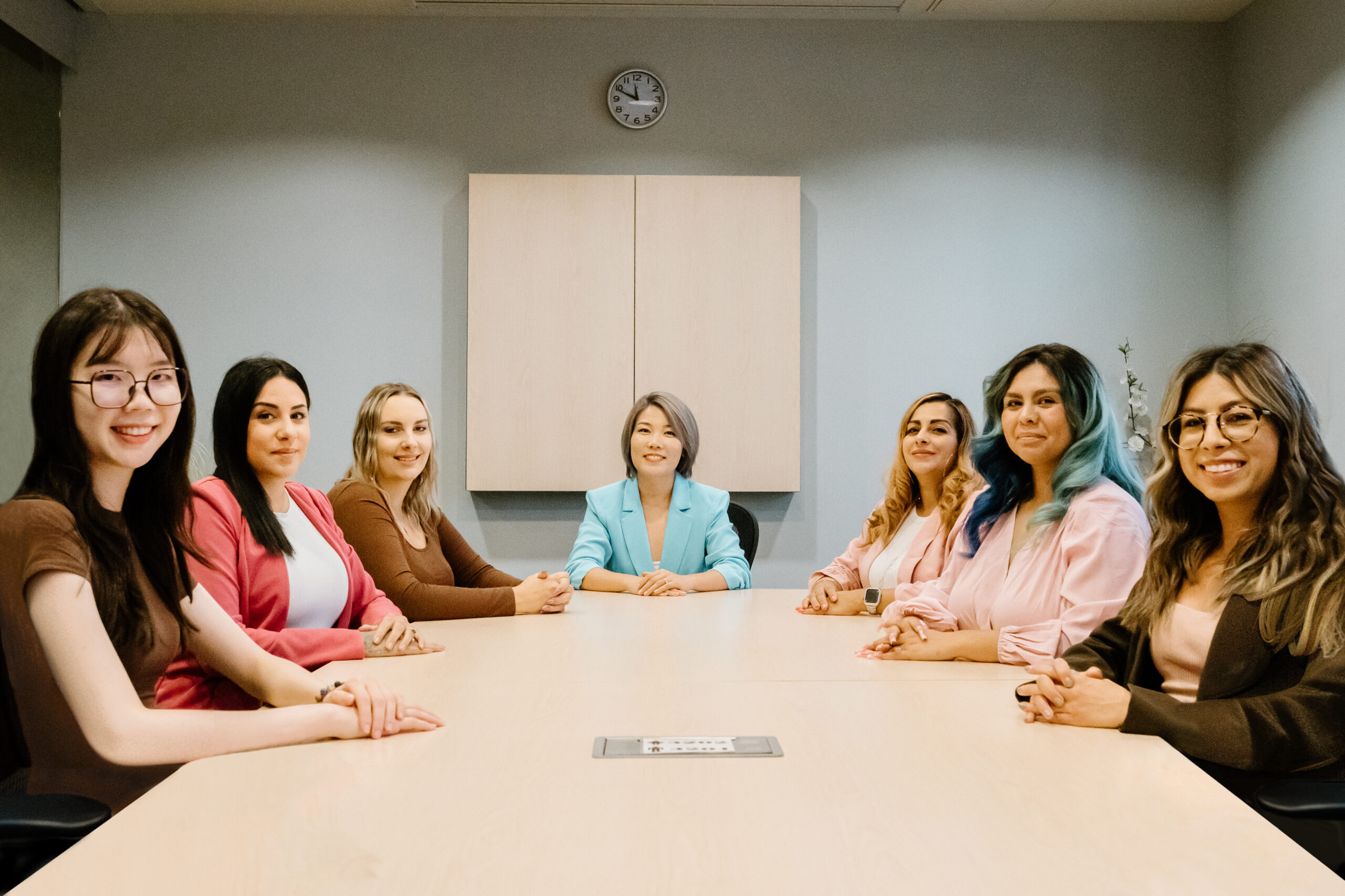 7 women sitting professionally at a table, smiling at the camera.