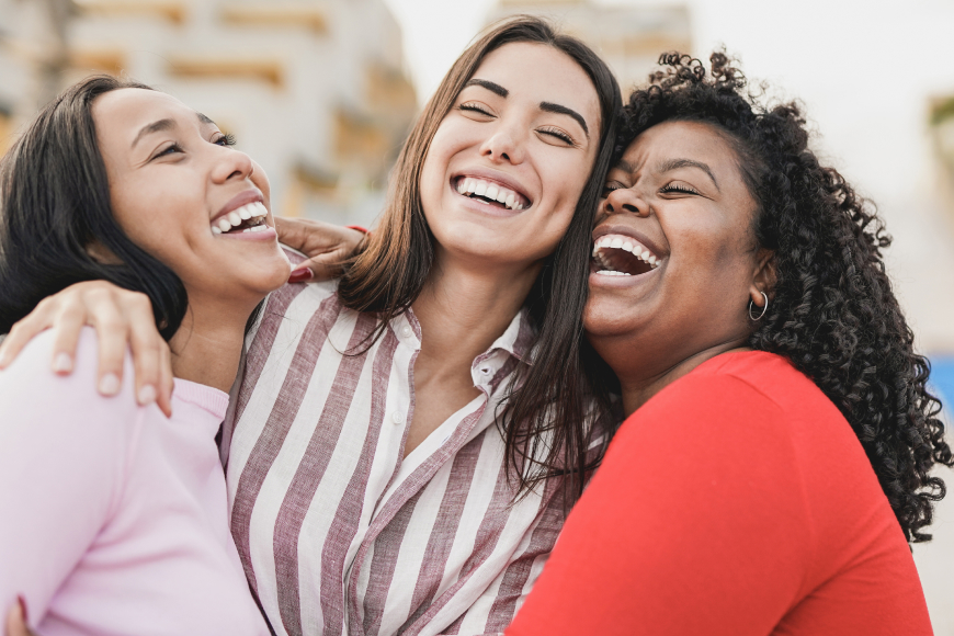 Felices mujeres latinas riendo y abrazándose al aire libre en la ciudad