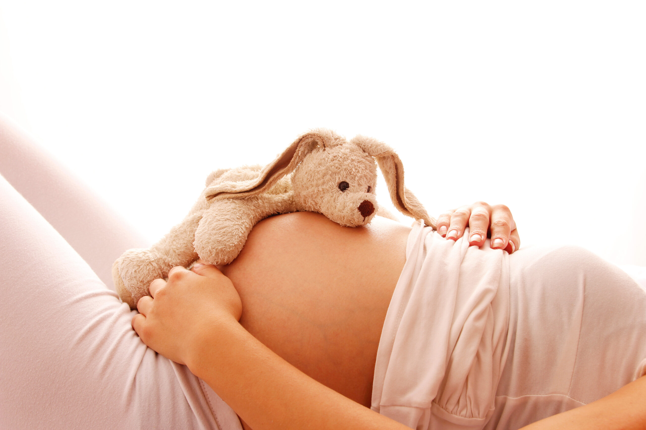 Pregnant woman lying down with a stuffed bunny resting on her belly.