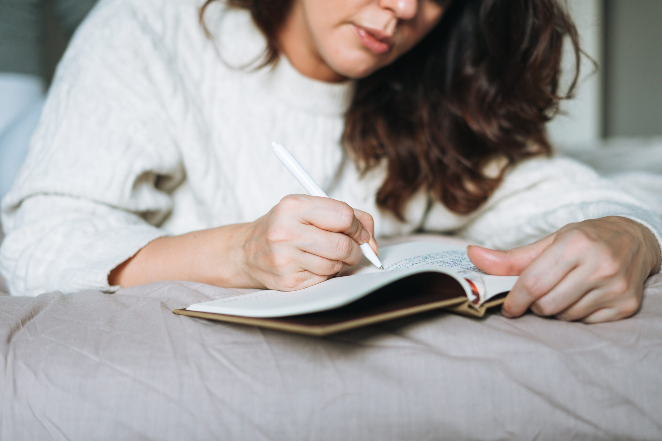 A women laying on her bed writing in a book.