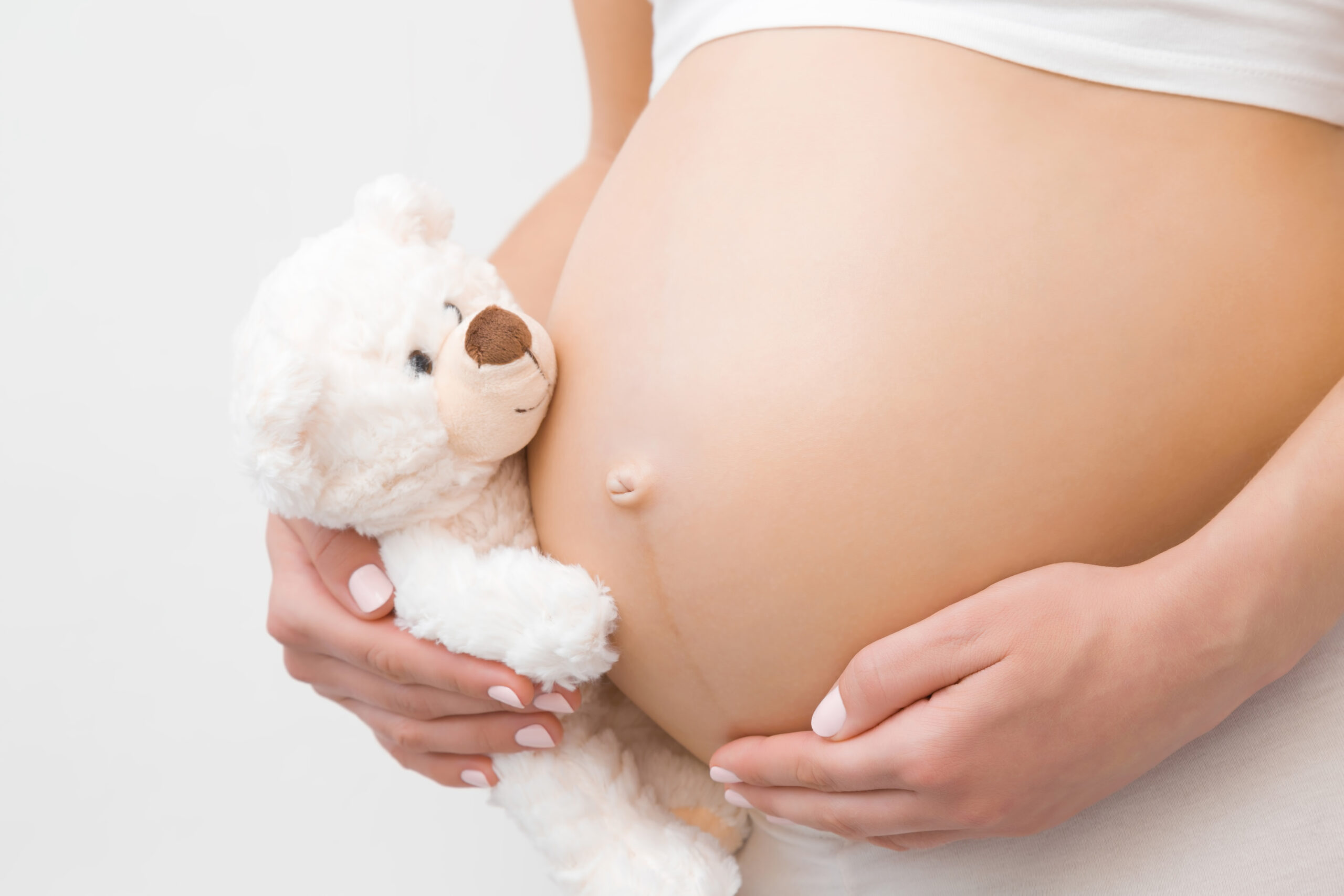 Pregnant woman with a white teddy bear on her stomach.