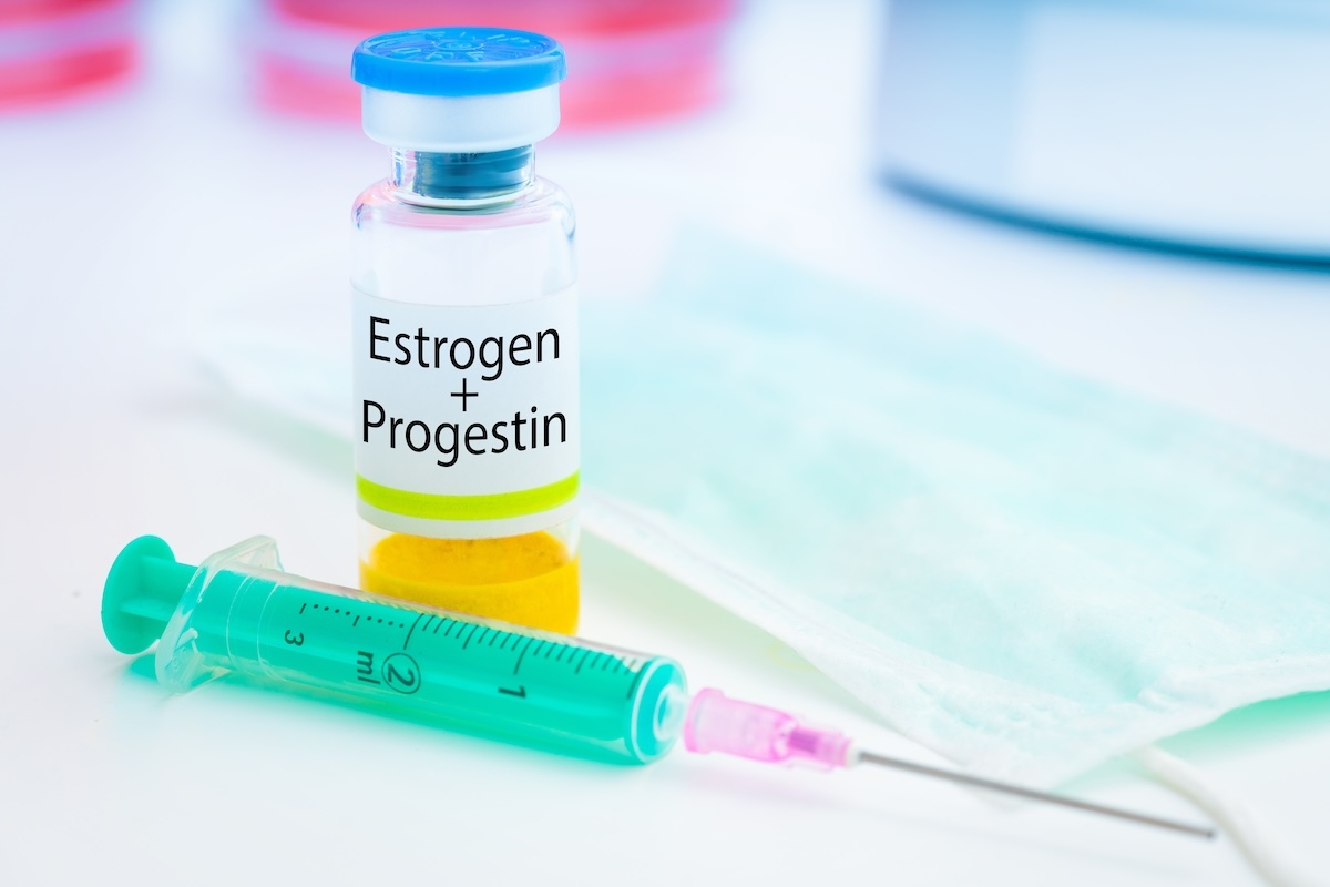 A vial labeled "Estrogen + Progestin" next to a syringe and a face mask on a white surface.