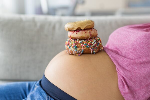 Pregnant woman with donuts on belly. Cravings of desserts and sweets during pregnancy, Girl eating unhealthy pastries on baby bump for gestational diabetes.