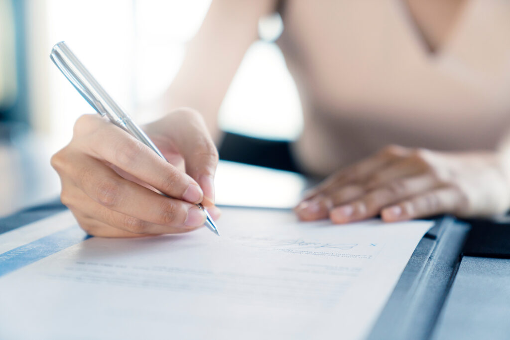 Close-up of a person signing a document with a pen on a clipboard.