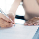 Close-up of a person signing a document with a pen on a clipboard.