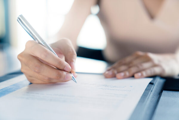 Close-up of a person signing a document with a pen on a clipboard.