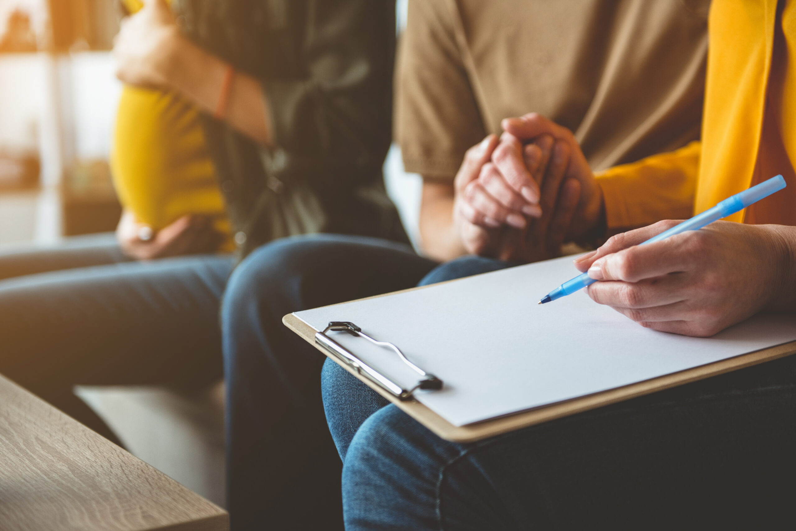 Close-up of intended parents holding hands and reviewing surrogacy paperwork while a pregnant surrogate sits nearby.