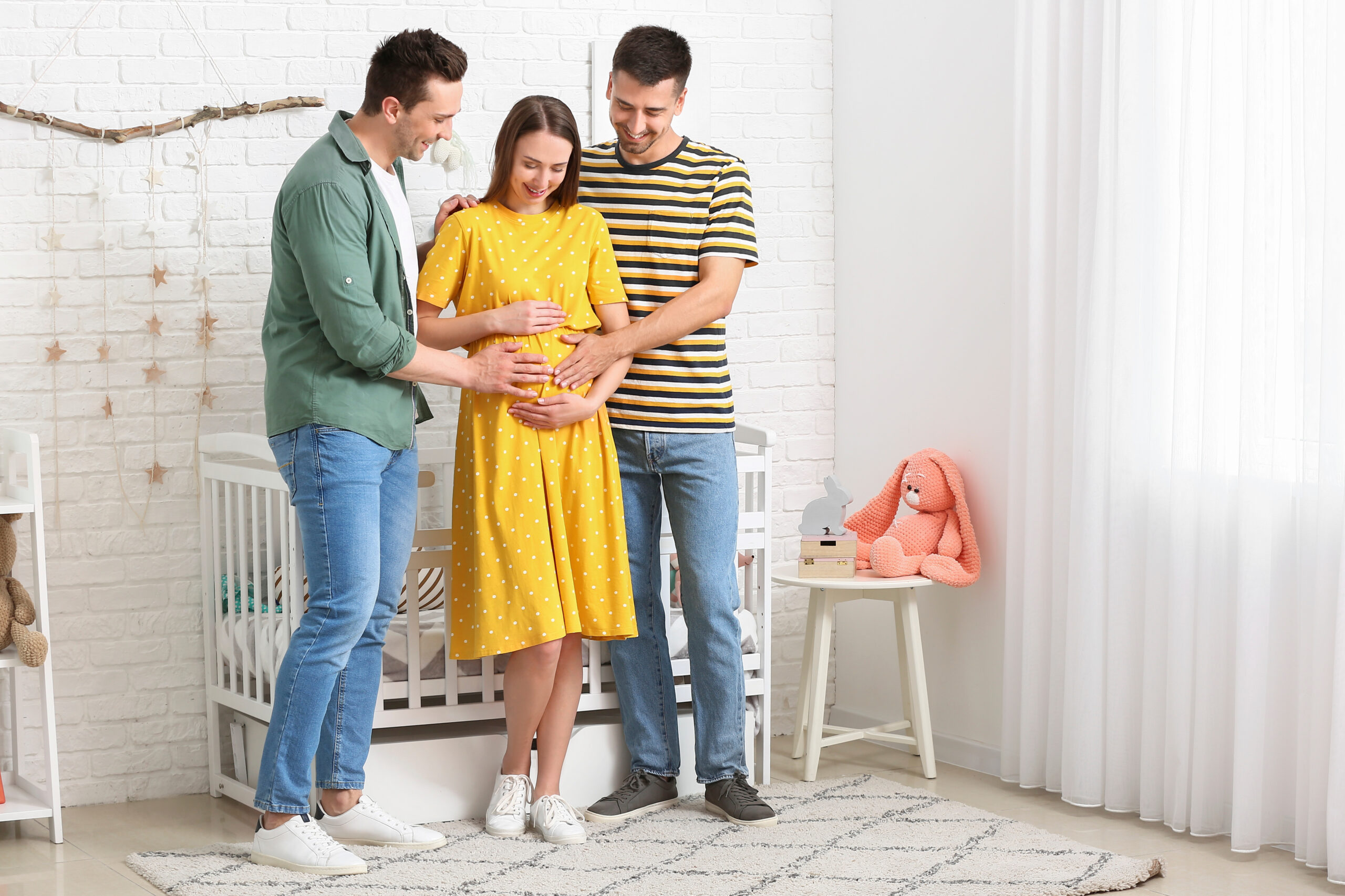 Two intended fathers embracing a surrogate mother with their hands on her baby bump.