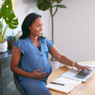 Pregnant woman smiling while using a laptop at a desk, researching surrogacy laws in a bright, modern home office.