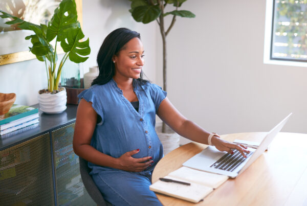 Pregnant woman smiling while using a laptop at a desk, researching surrogacy laws in a bright, modern home office.