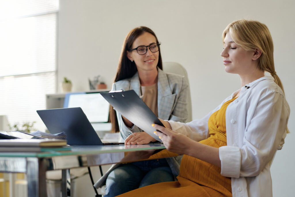 Pregnant woman reviewing documents with a lawyer in an office setting.
