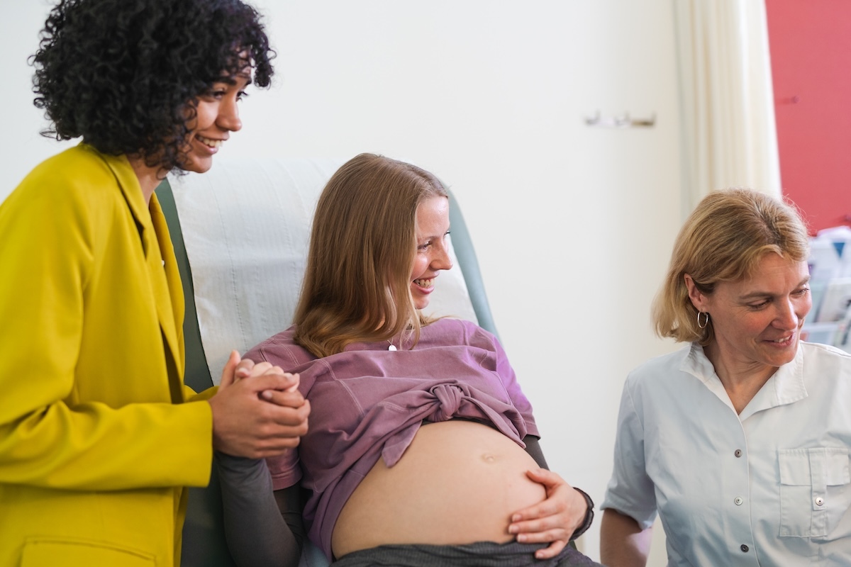 Pregnant woman smiling on a hospital bed, holding hands with her partner and surrounded by supportive medical staff.