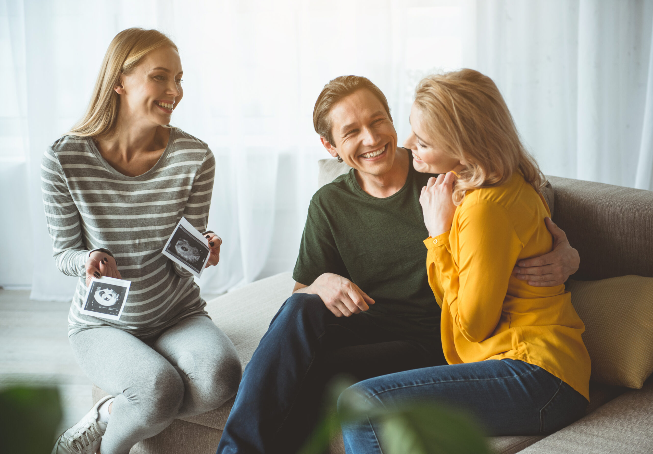 Surrogate sitting with intended parents, smiling and holding ultrasound photos during a joyful moment together.