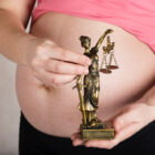 Pregnant woman in a pink top holding a small statue of Lady Justice, symbolizing the intersection of pregnancy and legal rights.