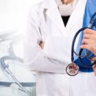 Does Insurance Cover Surrogacy? 5 Things to Know 2 Two healthcare professionals stand side by side, one in a white lab coat with arms crossed, and the other in blue scrubs holding a stethoscope. A stethoscope and an open laptop are visible on the table in the foreground.