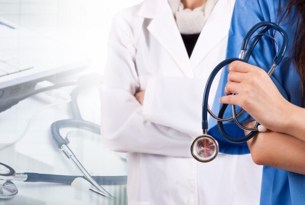 Does Insurance Cover Surrogacy? 5 Things to Know Two healthcare professionals stand side by side, one in a white lab coat with arms crossed, and the other in blue scrubs holding a stethoscope. A stethoscope and an open laptop are visible on the table in the foreground.