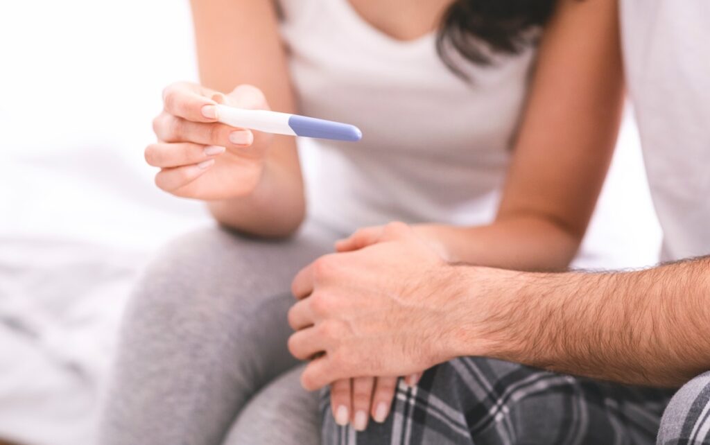 Person holding a pregnancy test while sitting beside a partner, reflecting a hopeful fertility or family-building moment.