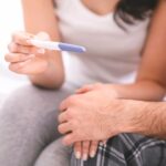 Person holding a pregnancy test while sitting beside a partner, reflecting a hopeful fertility or family-building moment.