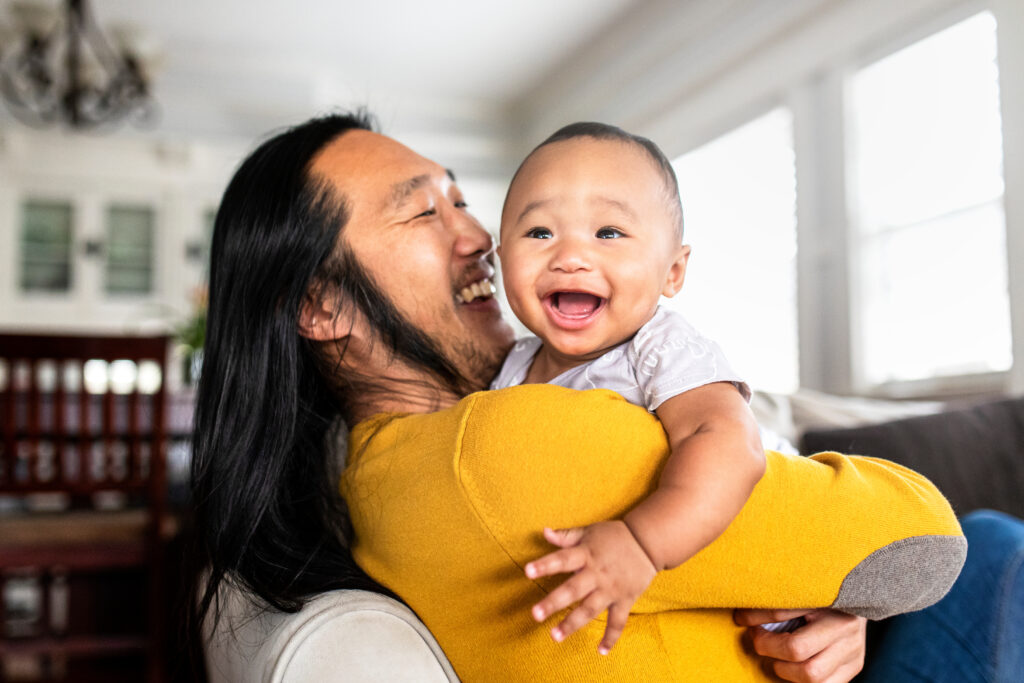 Smiling father holding a happy baby in a bright home, showing a warm parent-child moment.